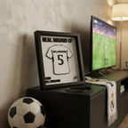 Cuadro camiseta Bellingham apoyado en el mueble del living junto a una bufanda del Real Madrid
